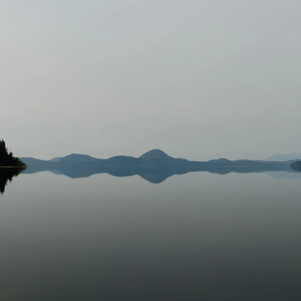 Mountains and shore reflected in a still lake (panel 1 of 4)