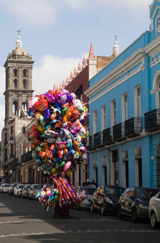 A balloon salesman pushing his cart down a cobblestone street
